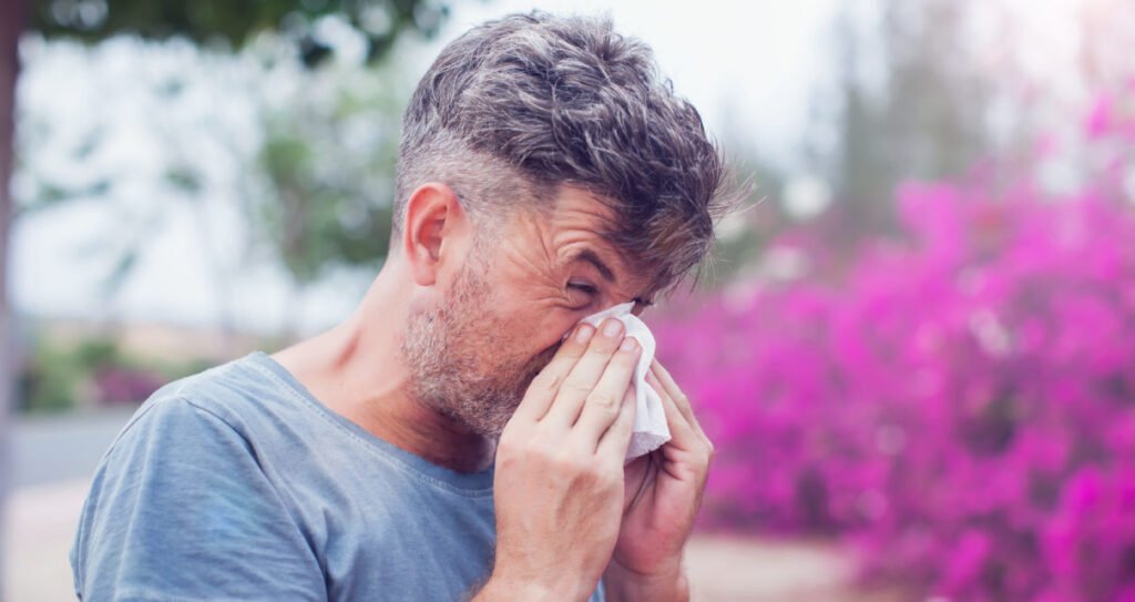 Man sneezing in a tissue outdoors. Pollen allergy, Springtime.