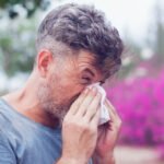 Man sneezing in a tissue outdoors. Pollen allergy, Springtime.