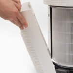 A man's hand turning an air purifier's filter into a new one.