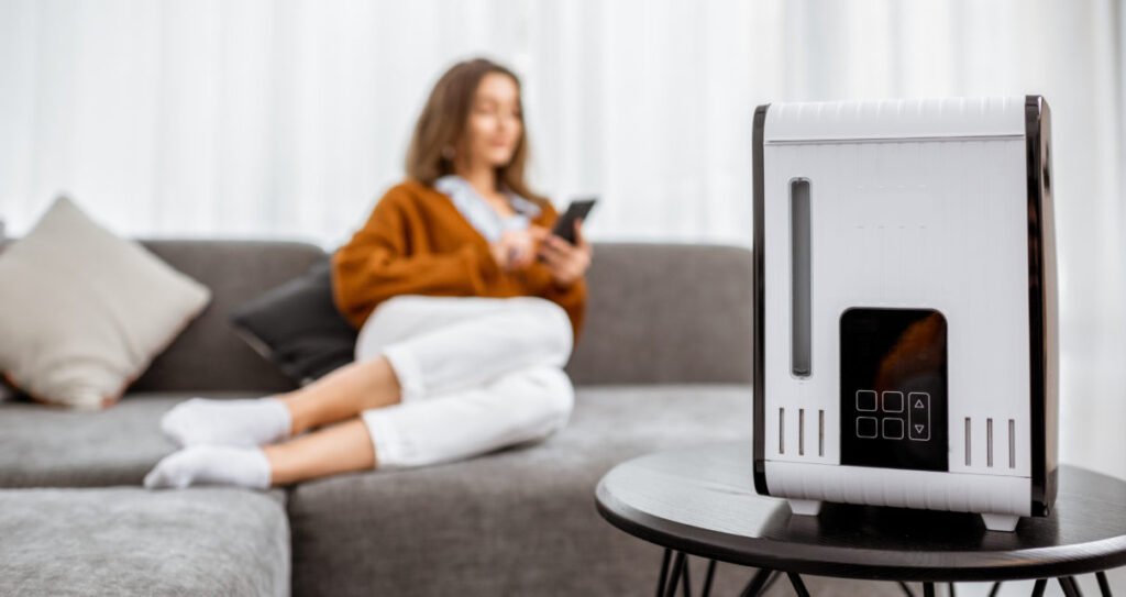 Young woman relaxing on the couch while air humidifier or purifier working on the foreground. Controlling it with a smartphone remotely