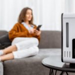 Young woman relaxing on the couch while air humidifier or purifier working on the foreground. Controlling it with a smartphone remotely