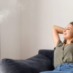 Attractive curly young woman using air humidifier at home