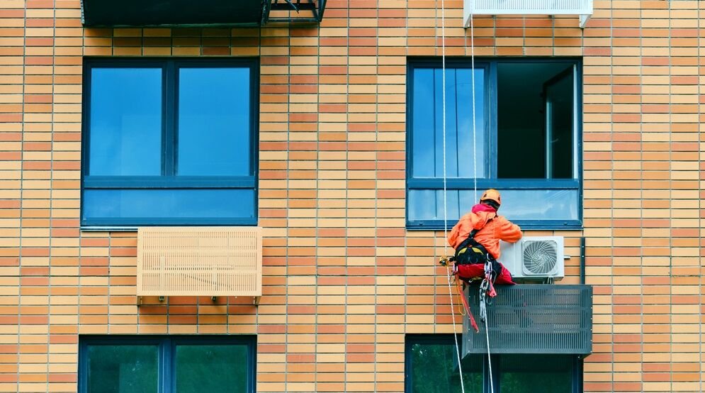 Industrial-climber-installs-air conditioning on the facade of an apartment building