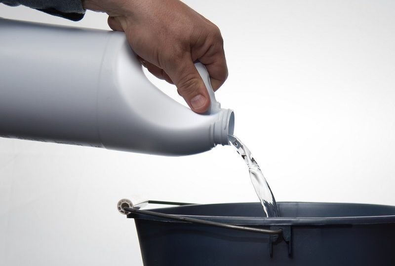 pouring cleaner or bleach into a blue bucket