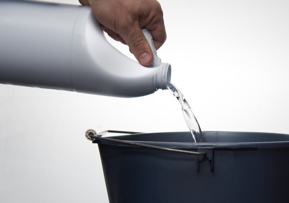 pouring cleaner or bleach into a blue bucket